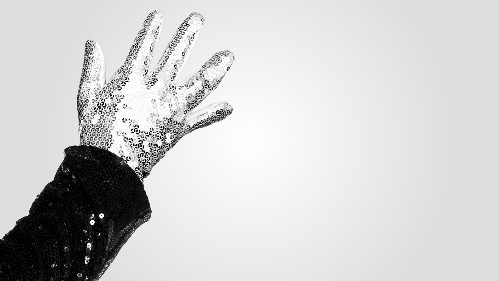 A raised arm, showing the bottom of a black sequined sleeve and a white sequined glove
